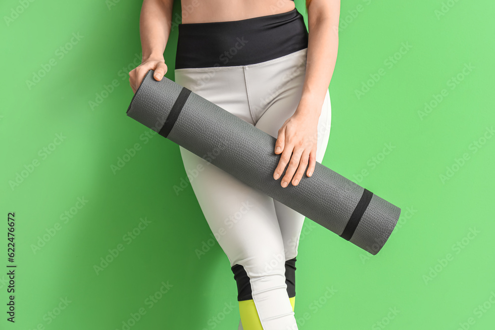 Young woman in sportswear and with yoga mat on green background