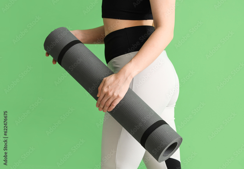 Young woman in sportswear and with yoga mat on green background