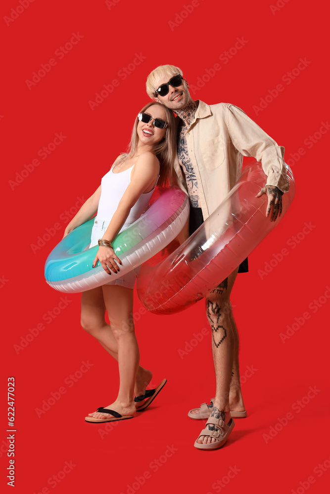 Young couple with inflatable rings on red background