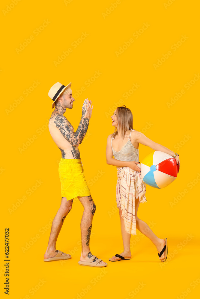 Young couple with beach ball on yellow background