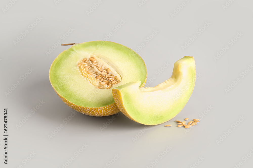 Half of sweet melon with piece and seeds on grey background