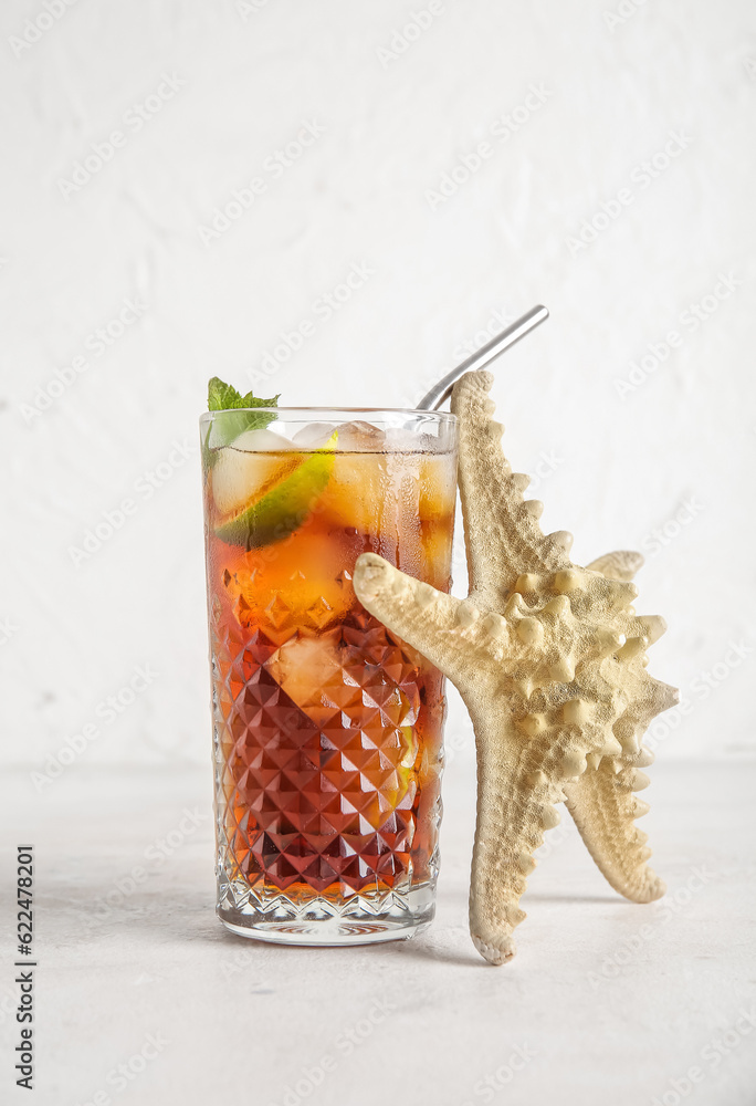 Glass of cold Cuba Libre cocktail and starfish on white background