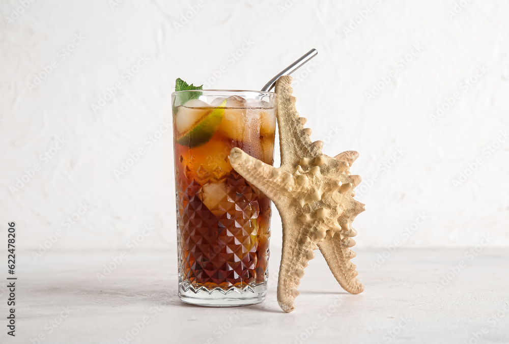 Glass of cold Cuba Libre cocktail and starfish on white background