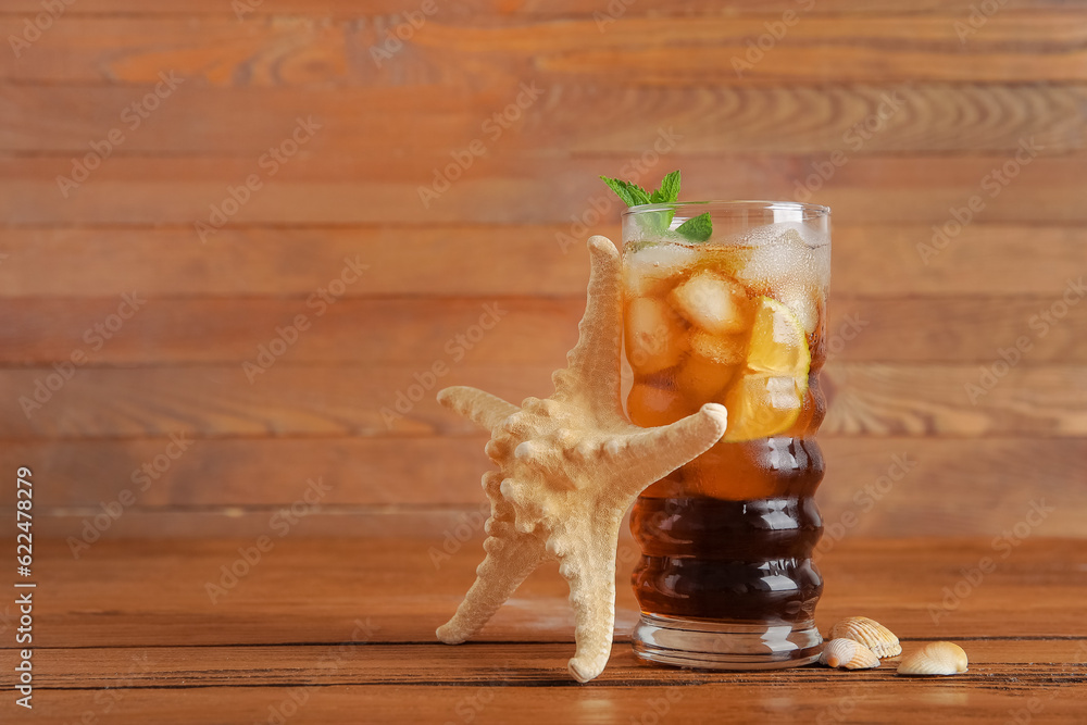 Glass of cold Cuba Libre cocktail, starfish and seashells on wooden background