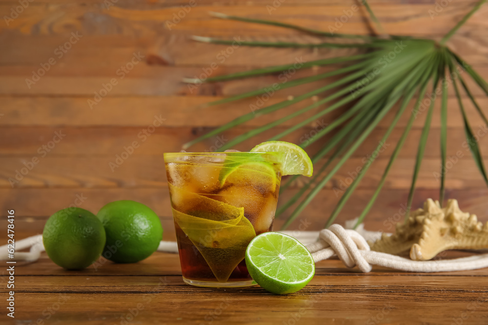 Glass of cold Cuba Libre cocktail and palm leaf on wooden background