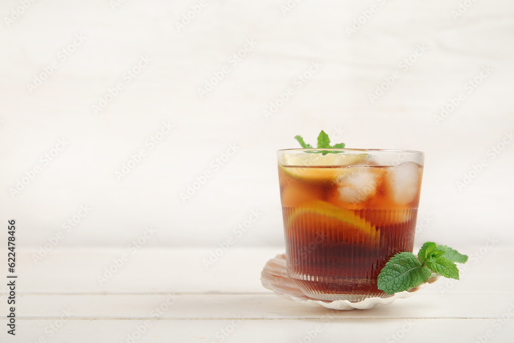 Glass of cold Cuba Libre cocktail and seashell on white wooden table