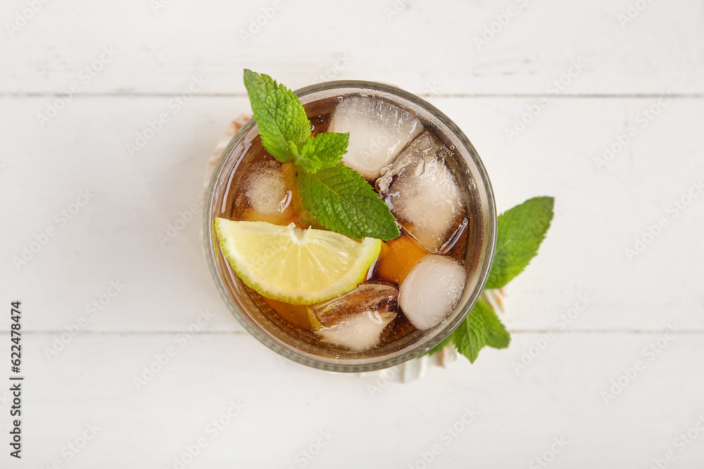 Glass of cold Cuba Libre cocktail on white wooden background