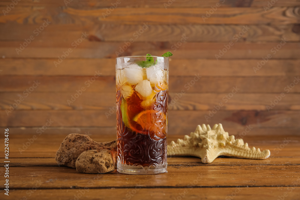 Glass of cold Cuba Libre cocktail, starfish and stones on wooden background