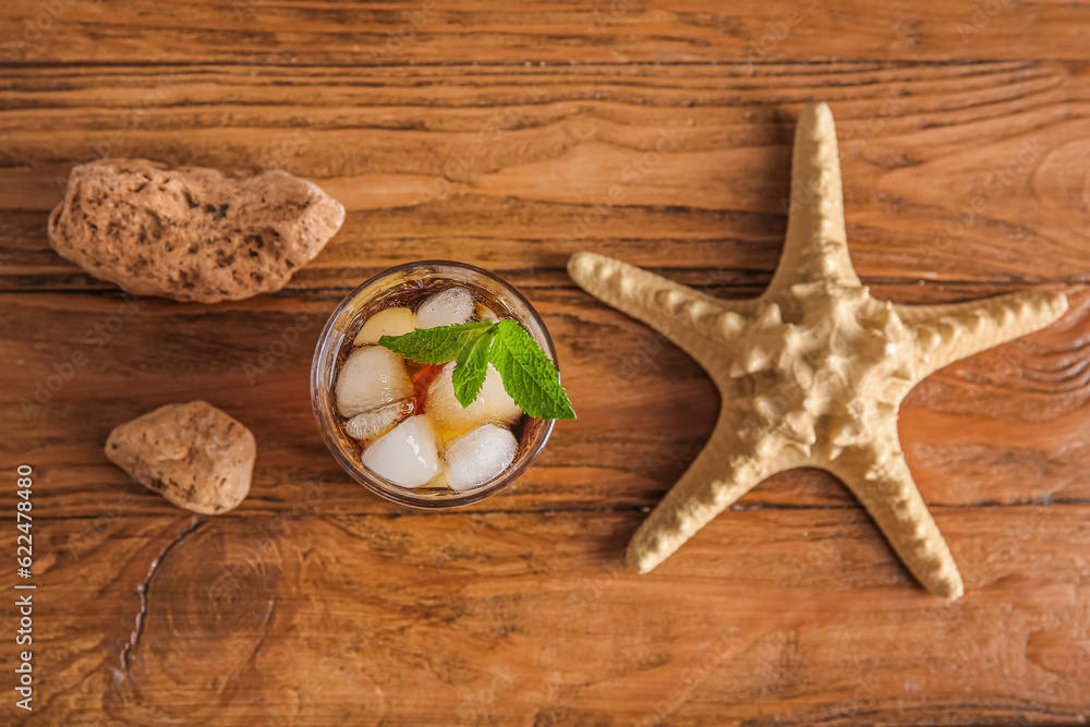 Glass of cold Cuba Libre cocktail, starfish and stones on wooden background