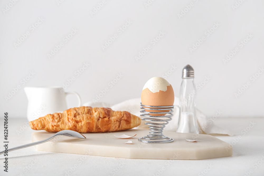 Holder with boiled chicken egg and croissant on white background