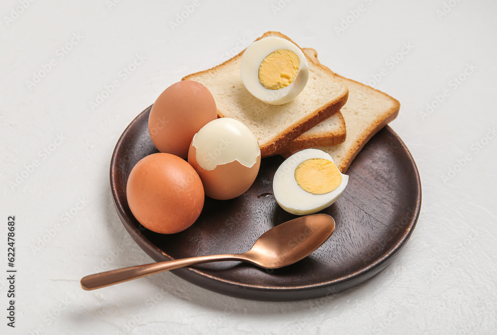 Plate with boiled chicken eggs and bread on white background