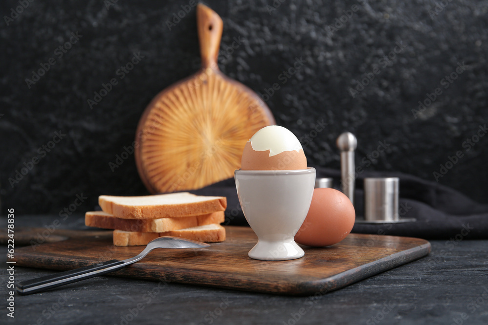 Holder with boiled chicken egg and bread on black background