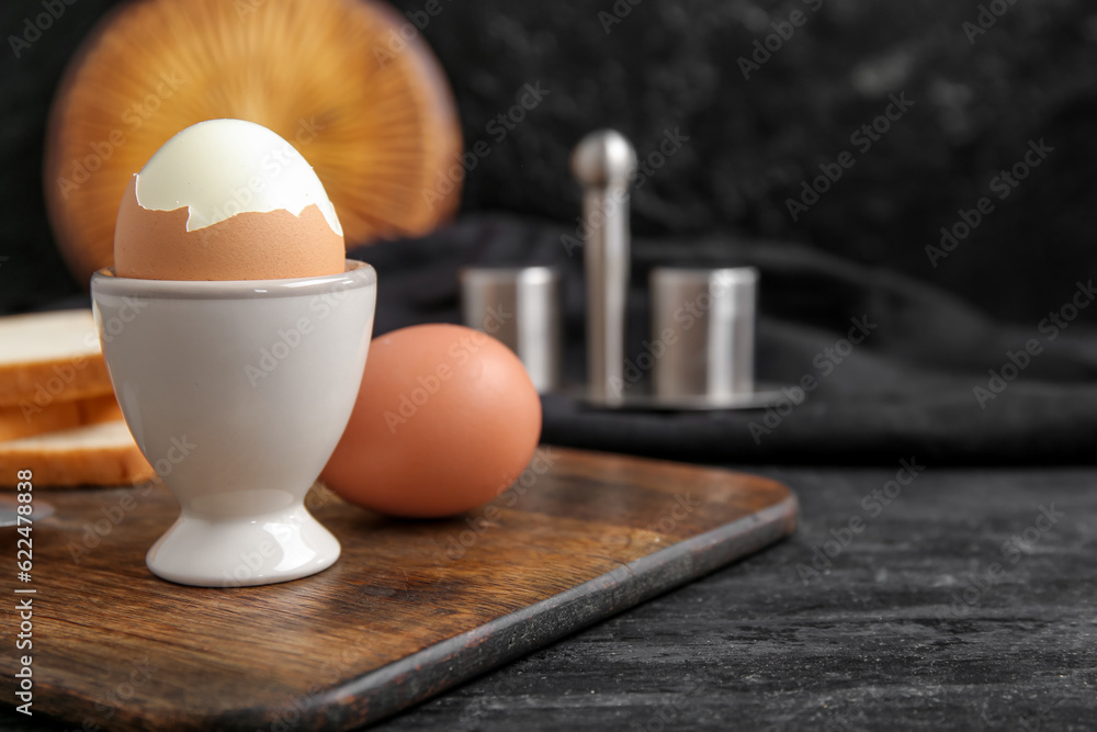 Holder with boiled chicken egg on black background