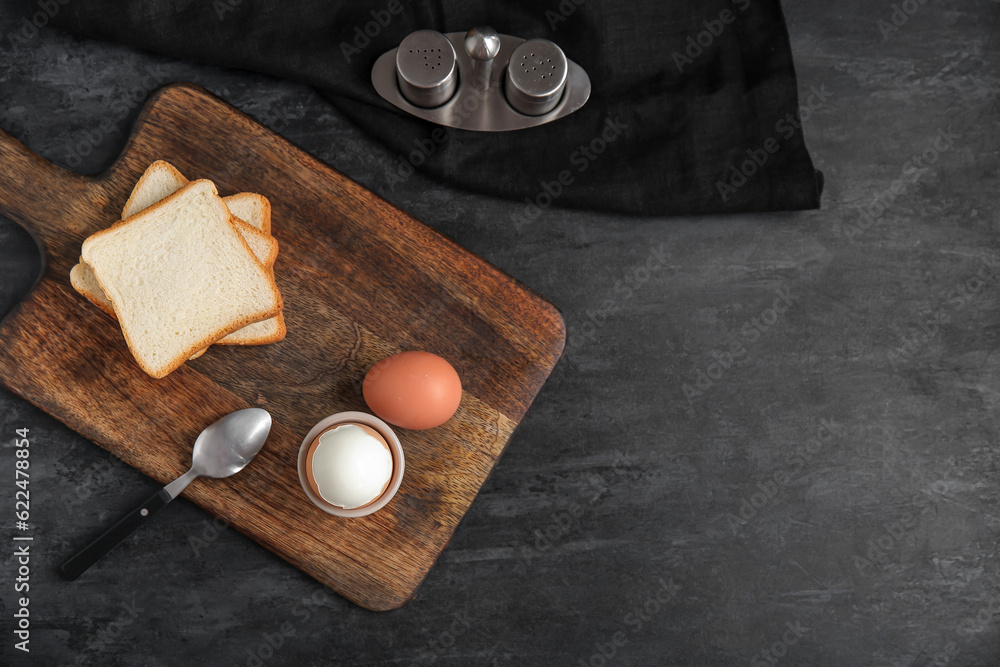 Holder with boiled chicken egg and bread on black background