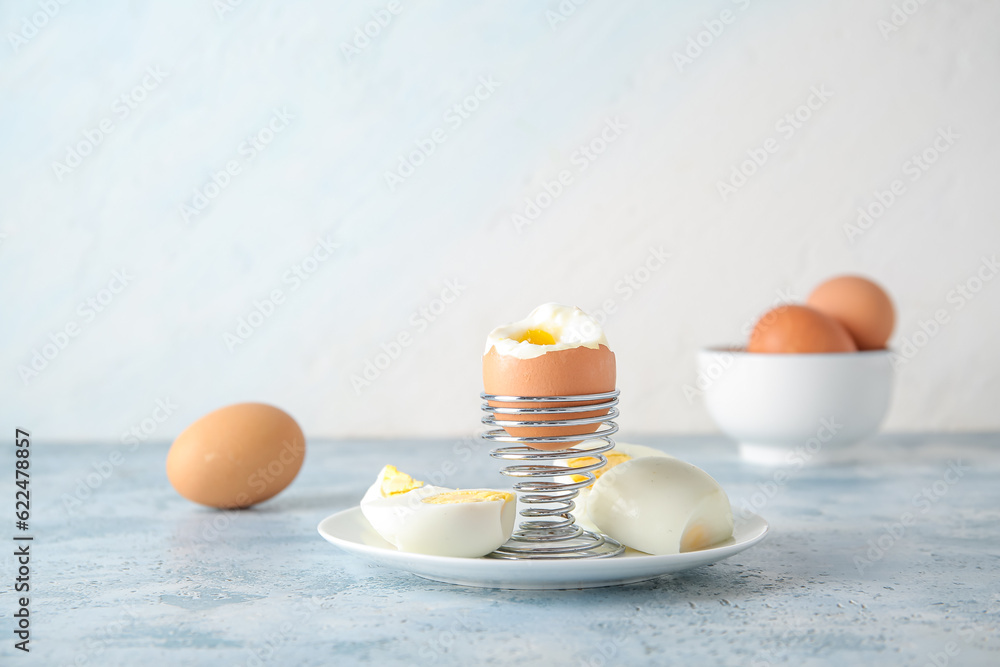 Holder with boiled chicken egg on blue table