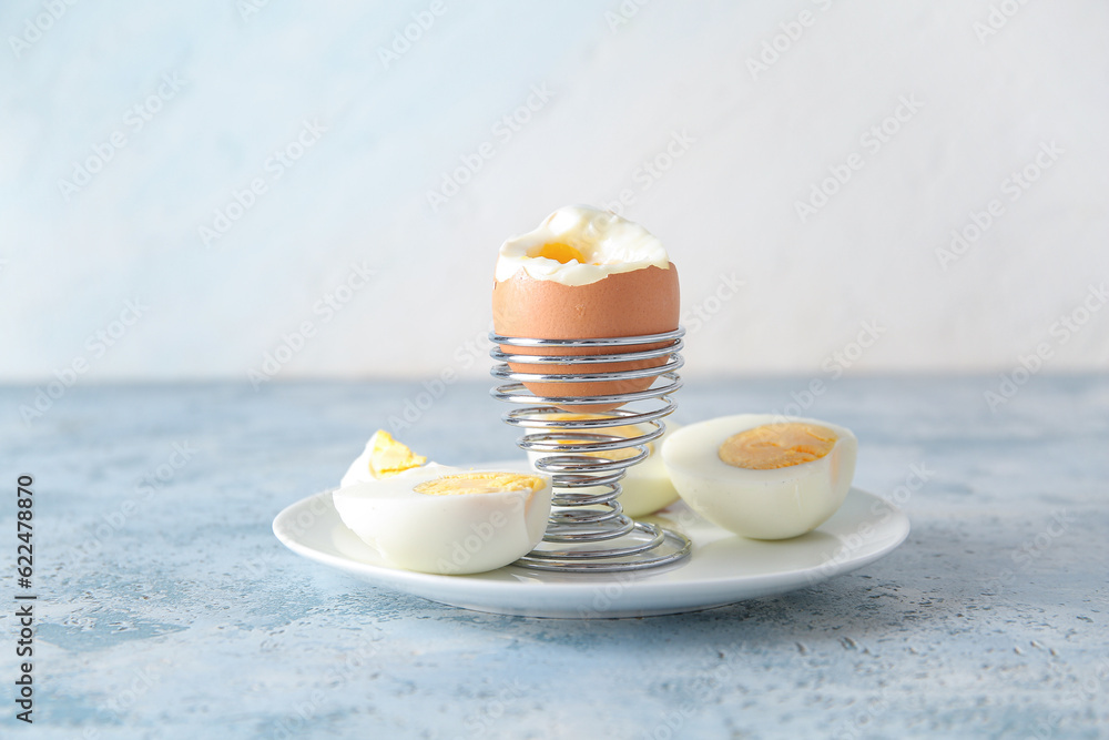 Holder with boiled chicken egg on blue table