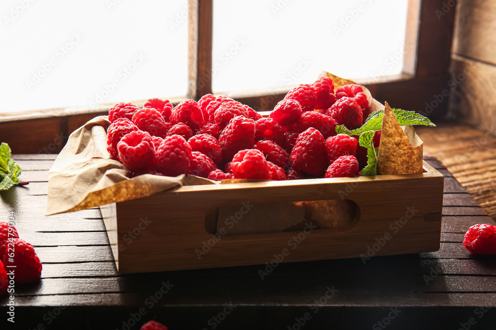 Wooden box with fresh raspberries on windowsill