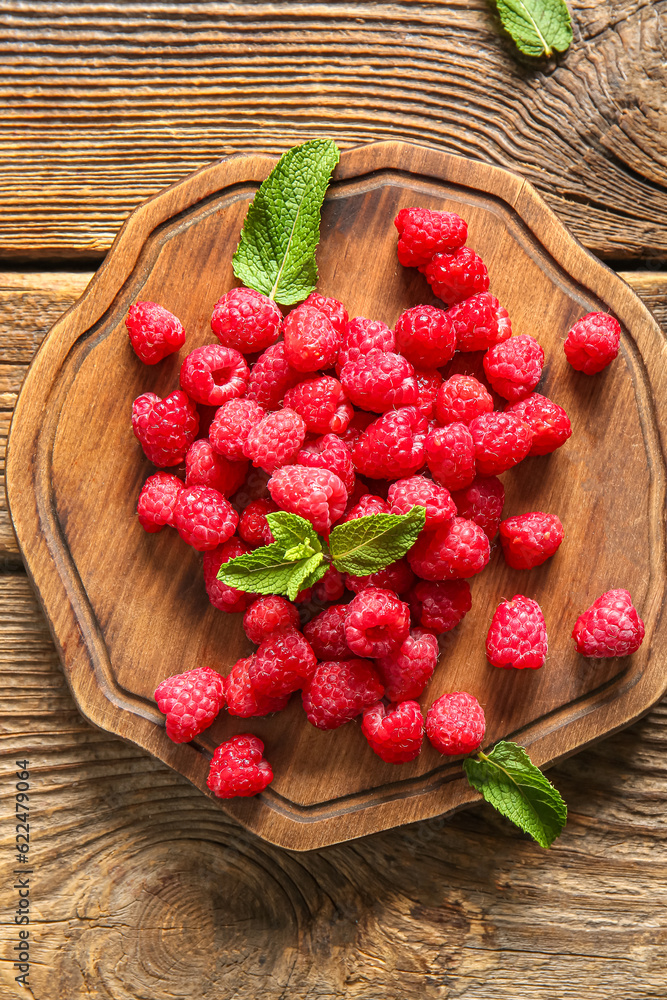 Board with fresh raspberries and mint on wooden background