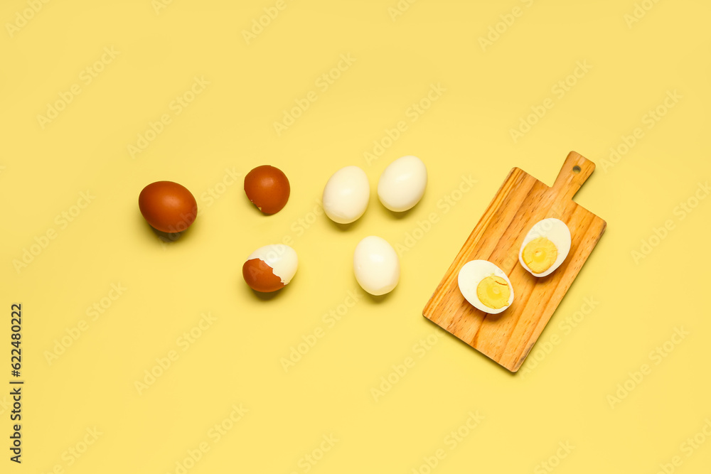 Tasty boiled eggs and wooden board with halves on yellow background