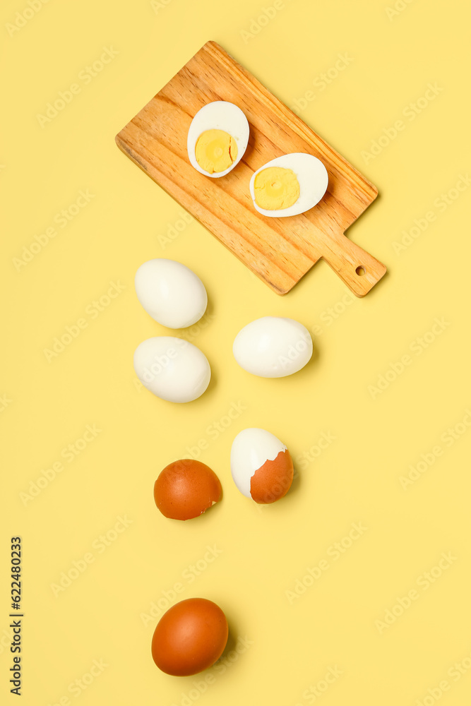 Tasty boiled eggs and wooden board with halves on yellow background