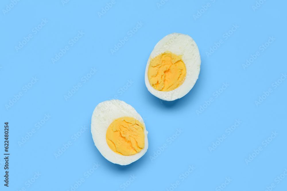 Halves of tasty boiled egg on blue background