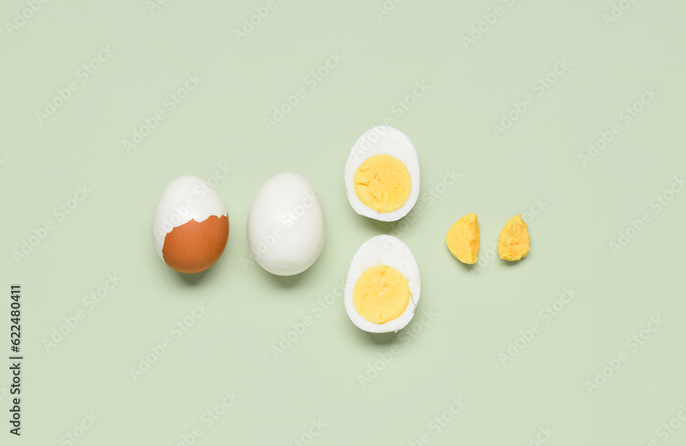 Tasty boiled eggs with halves on green background