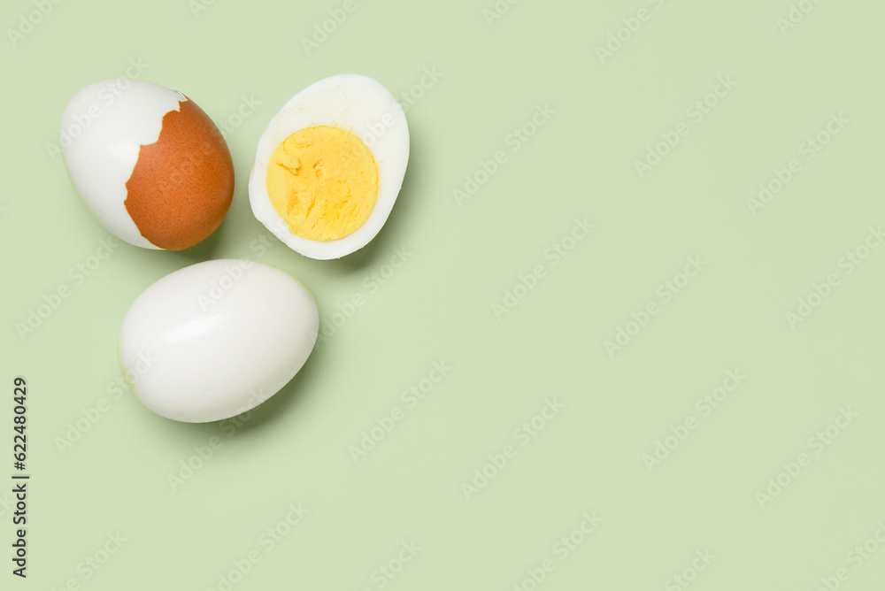 Tasty boiled eggs with half on green background