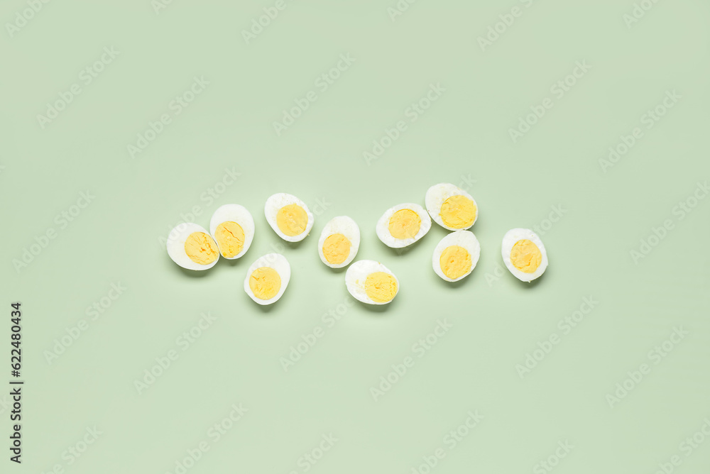 Halves of tasty boiled eggs on green background