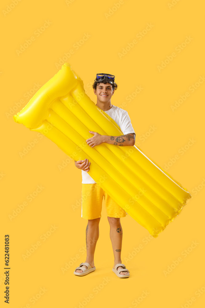 Young man with swim mattress on yellow background