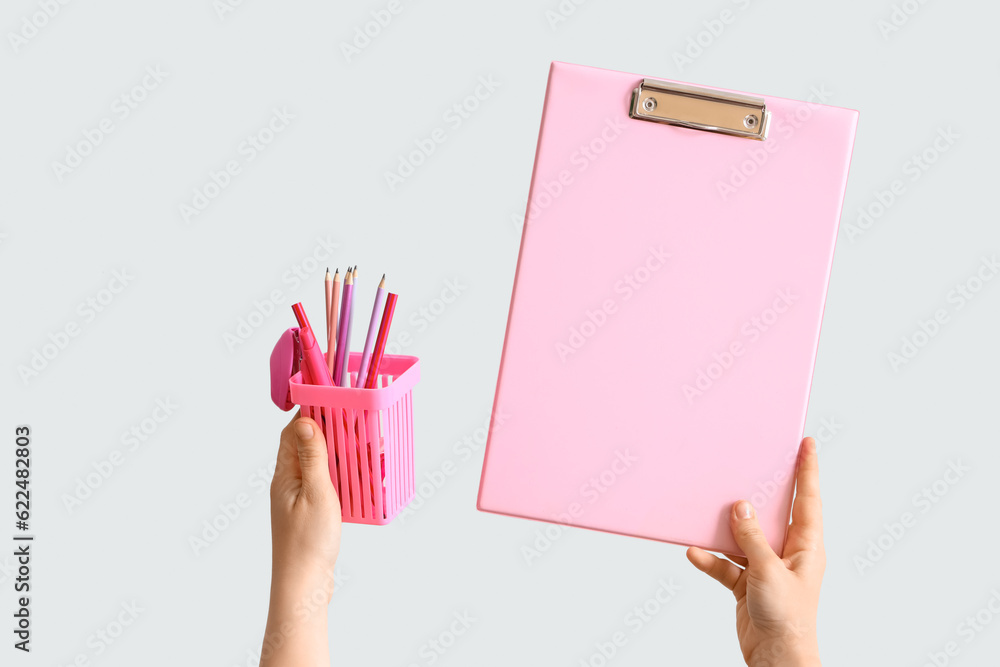 Female hands holding pen cup and clipboard on grey background