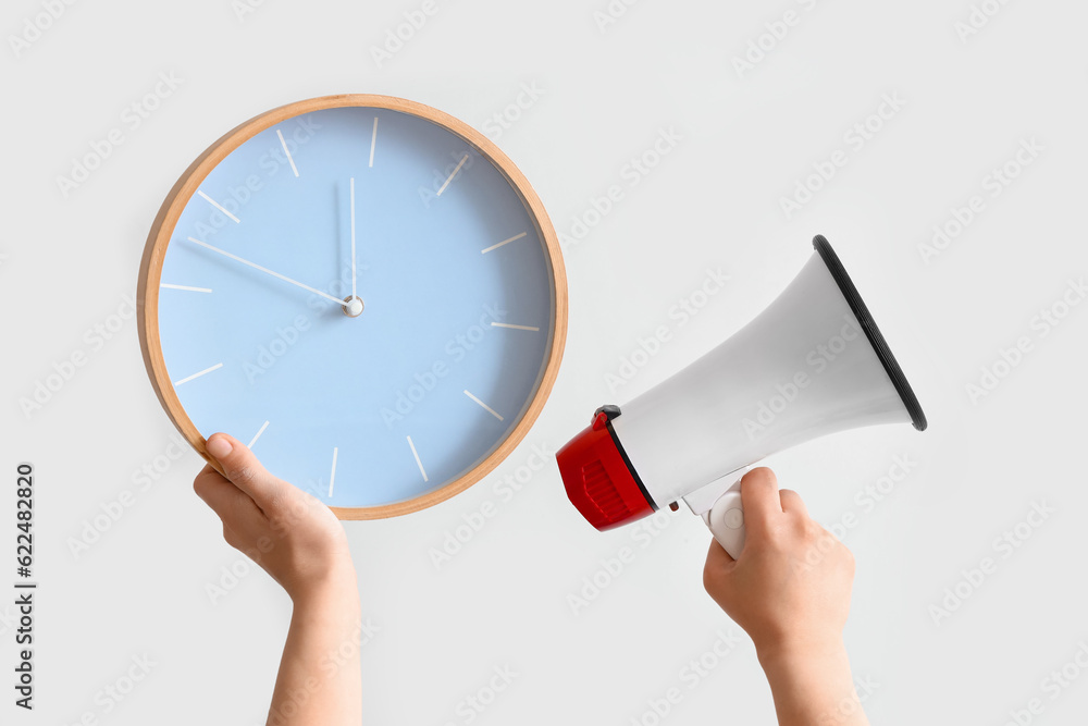 Female hands holding clock and megaphone on grey background