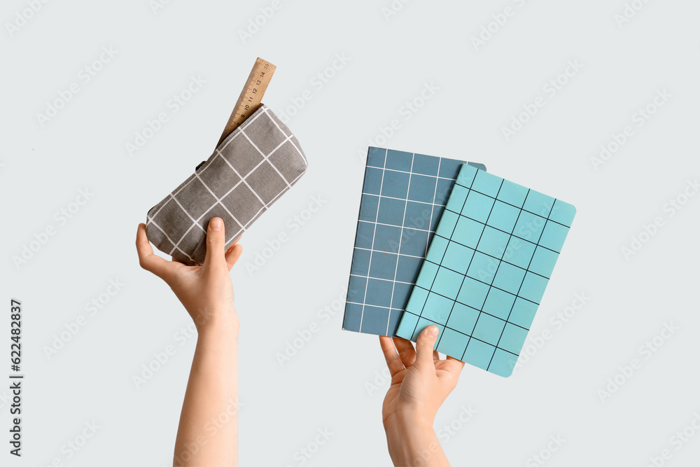 Female hands holding pencil case and copybooks on grey background