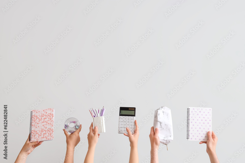 Many hands holding school supplies on grey background