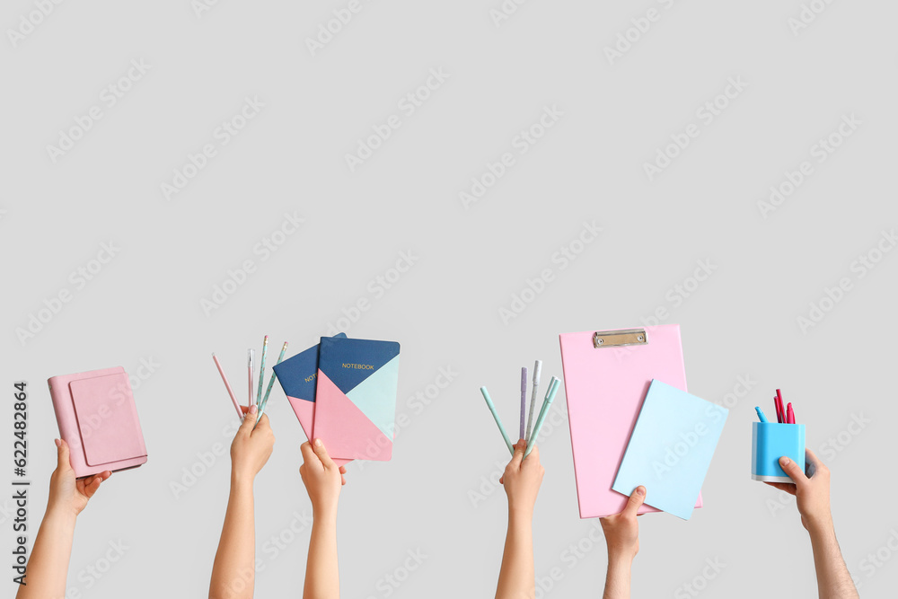 Many hands holding school supplies on grey background