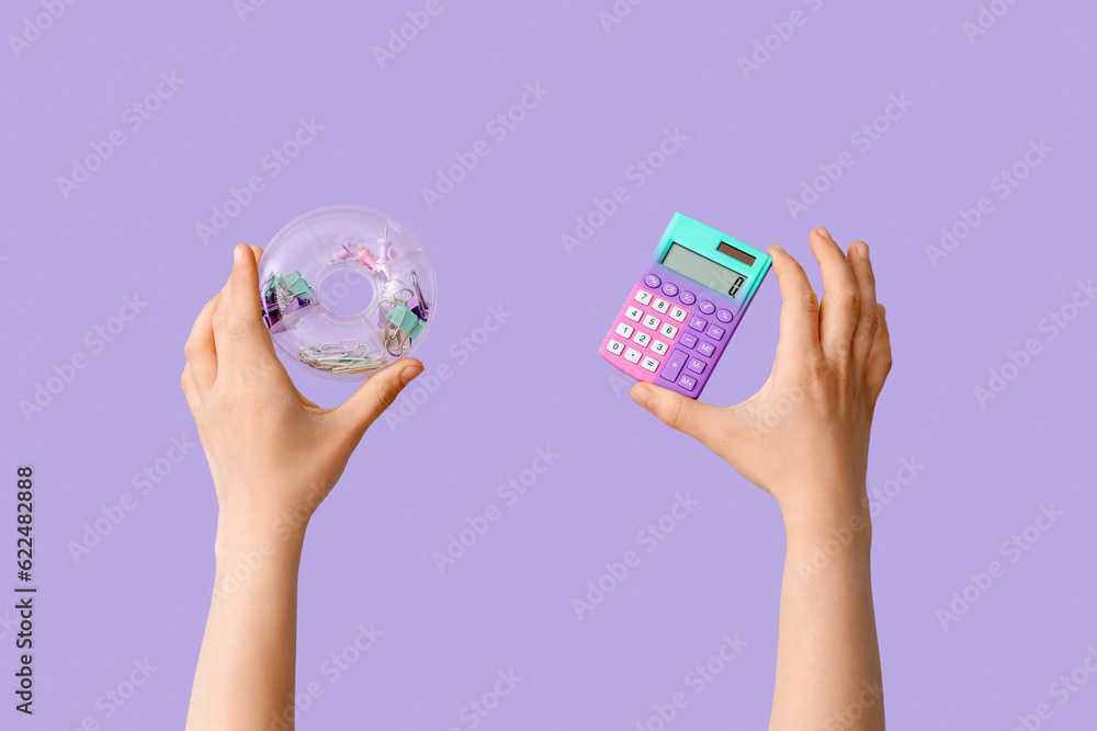 Female hands holding stationery case and calculator on lilac background