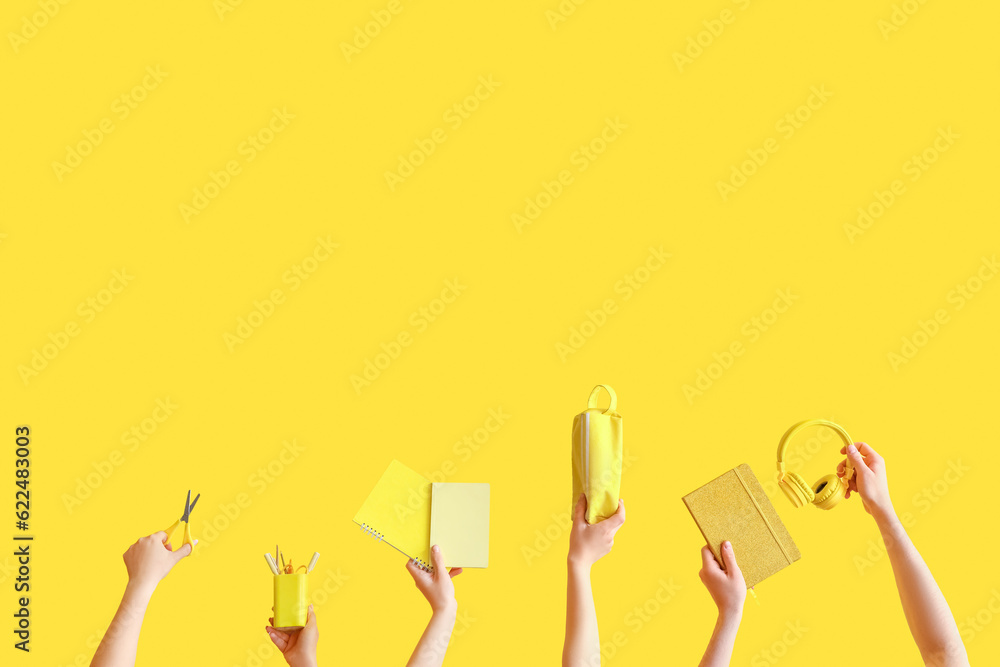 Many hands holding school supplies on yellow background