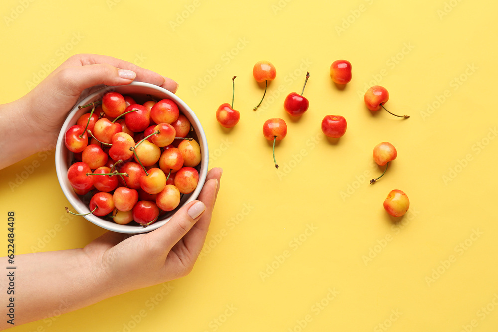 Woman holding bowl with sweet yellow cherries on color background