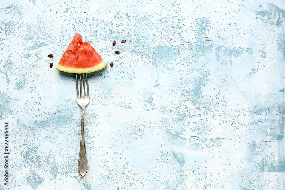 Fork with piece of fresh watermelon and seeds on blue background