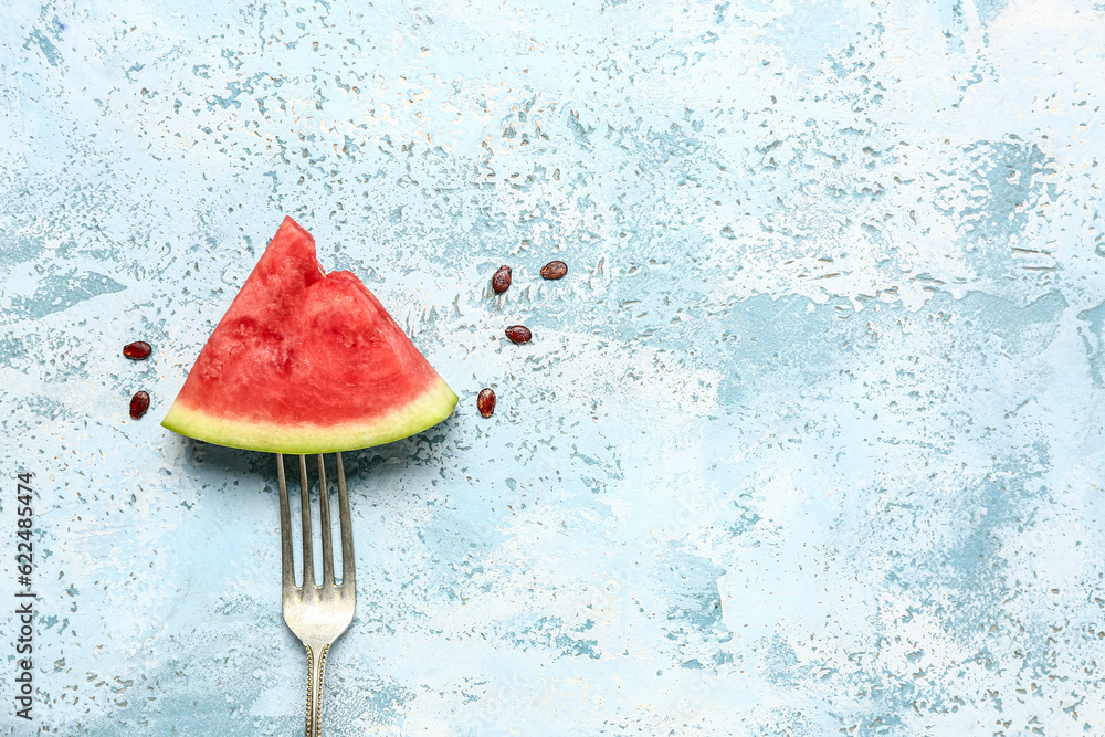 Fork with piece of fresh watermelon and seeds on blue background