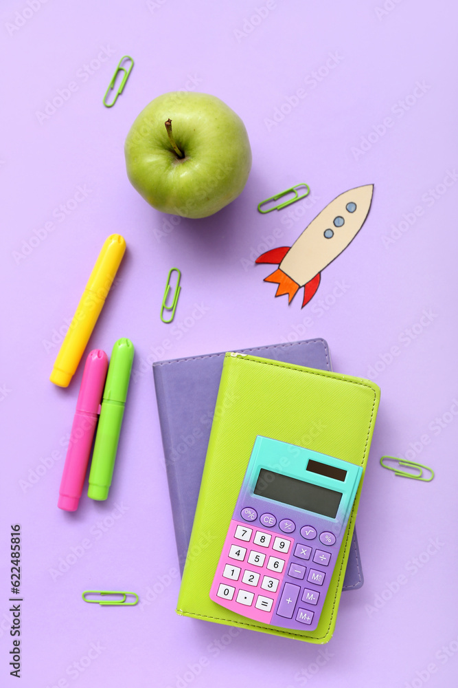 Paper rocket with school stationery and apple on purple background