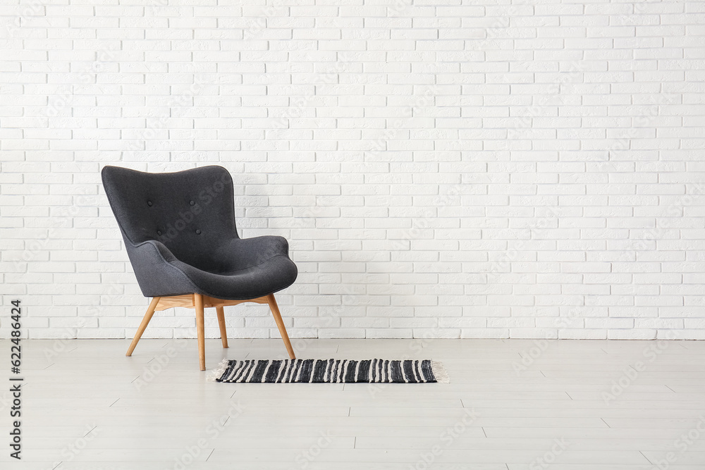 Stylish black armchair and carpet near white brick wall