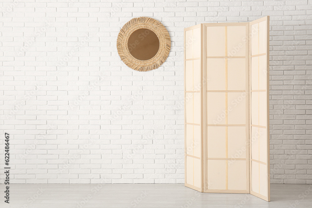 Folding screen and mirror near white brick wall