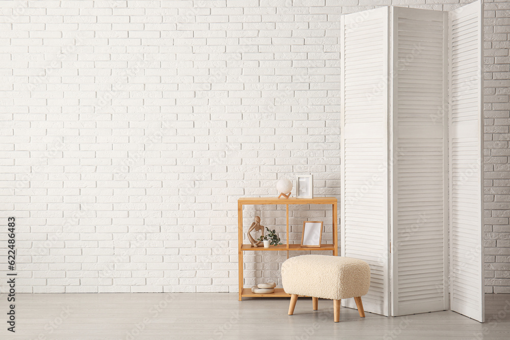 Folding screen with shelving unit and ottoman near white brick wall