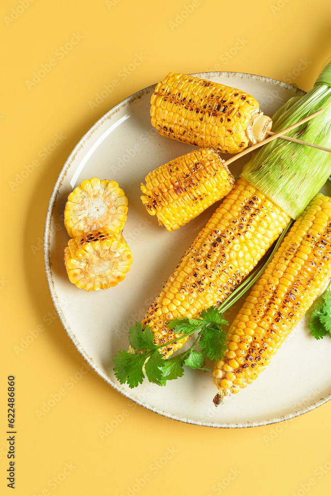 Plate with tasty grilled corn cobs and parsley on yellow background