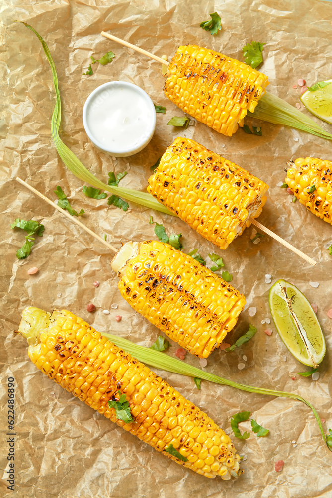 Baking paper with tasty grilled corn cob skewers and sauce, closeup