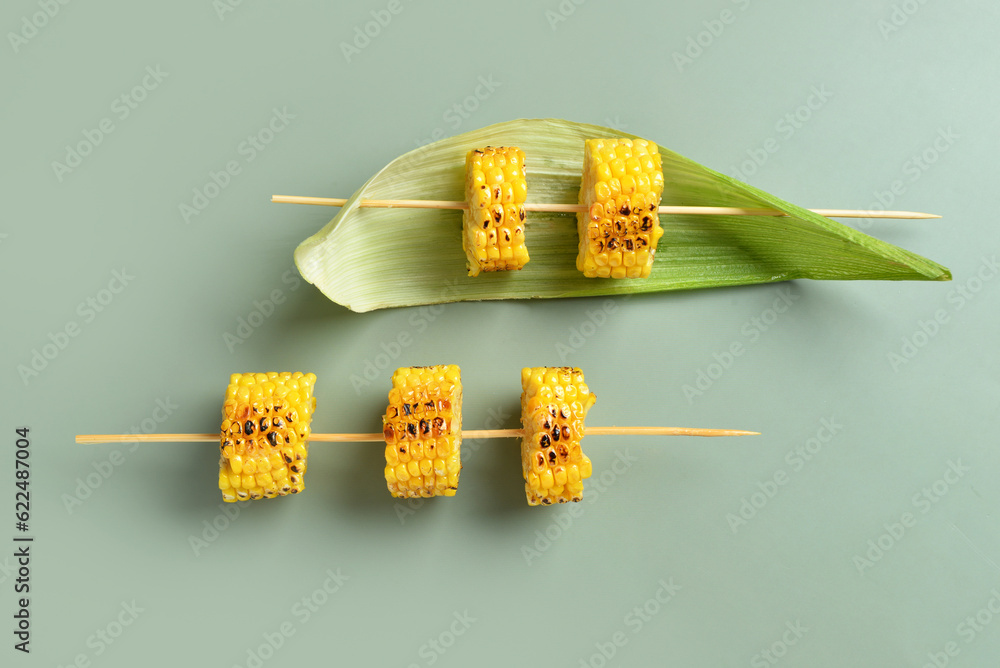 Tasty grilled corn cob skewers on green background