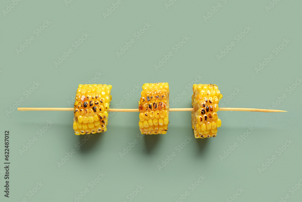 Tasty grilled corn cob skewer on green background