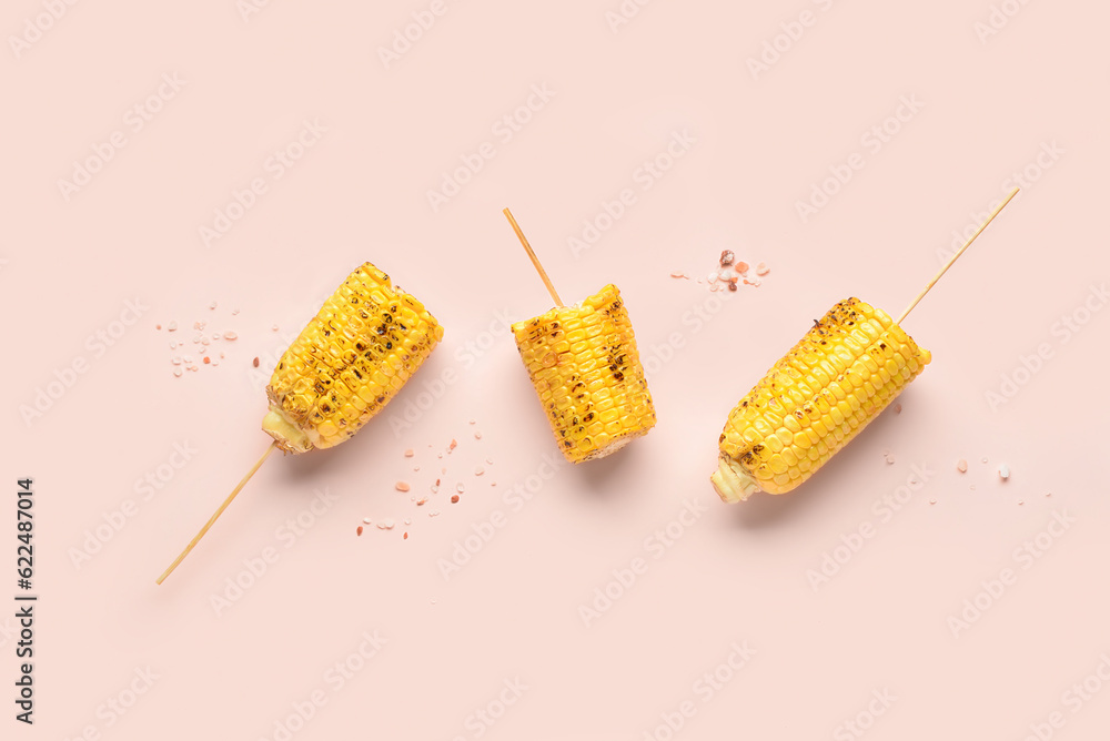 Tasty grilled corn cob skewers on pink background