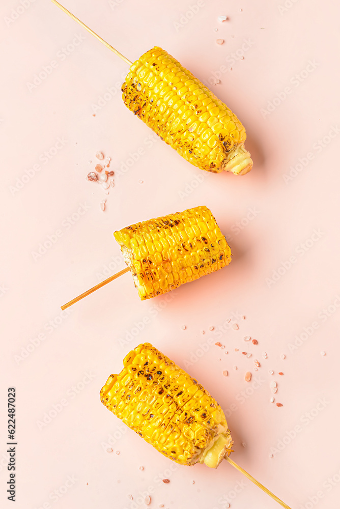 Tasty grilled corn cob skewers on pink background