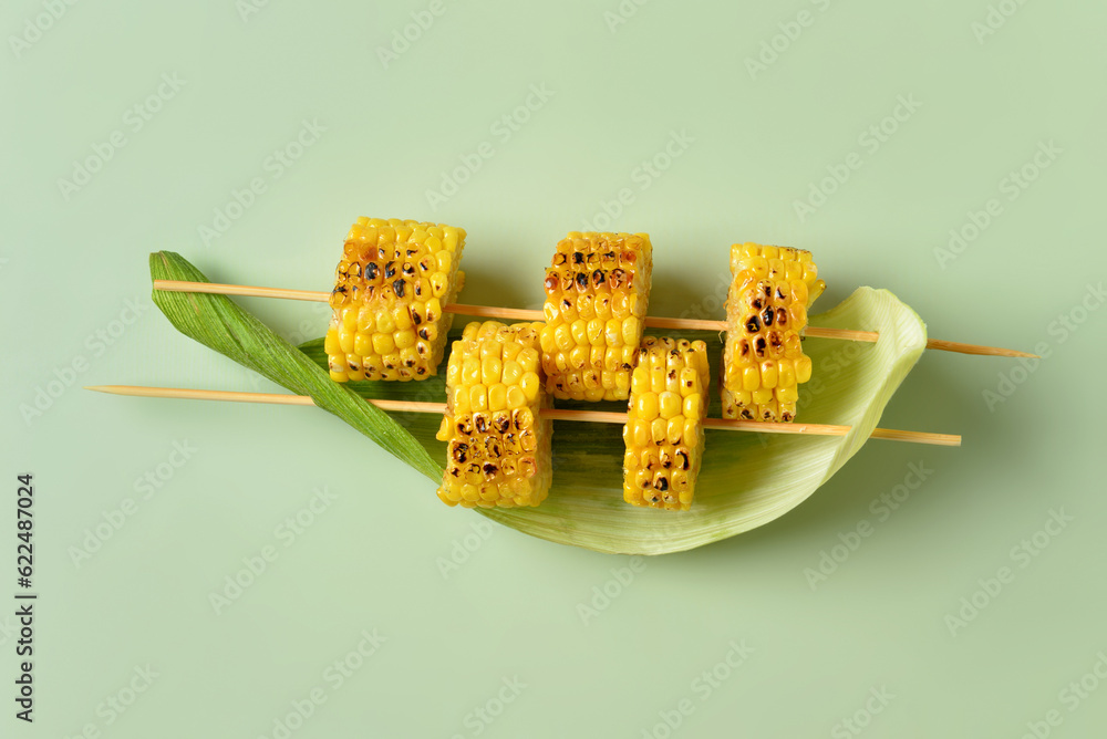 Tasty grilled corn cob skewers on green background